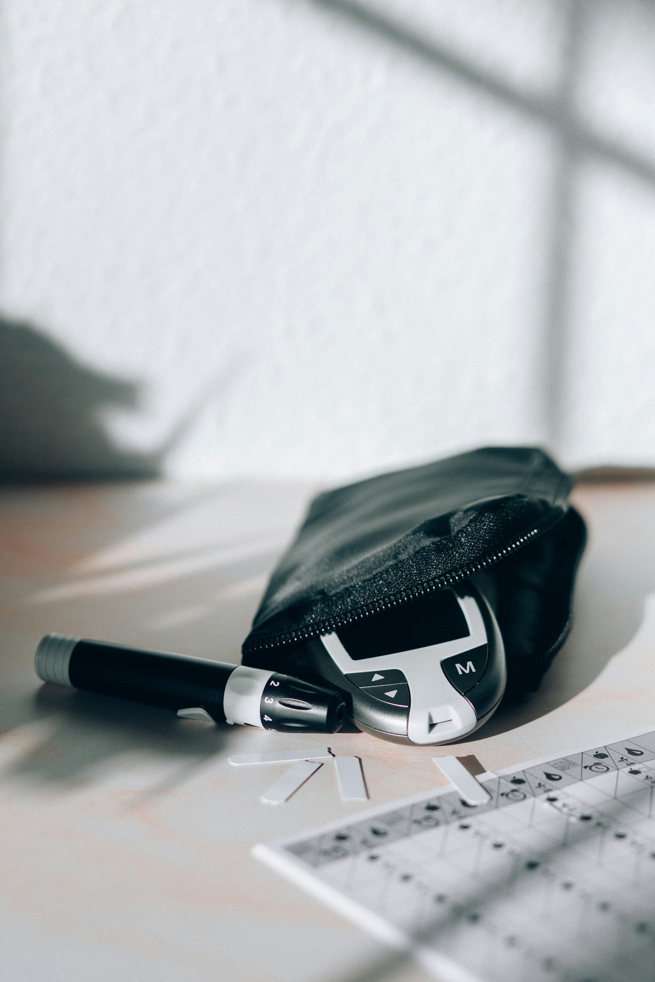What we cover in each Diabetes Reset session: a black‑and‑white diabetes test kit featuring a glucose meter, lancet device, and test strips on a sunlit table.