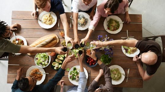 Overhead view of a diverse group sharing healthy salads, bread, and drinks in a communal toast—illustrating What Makes the 90‑Day Intensive Unique in personalized coaching through community, accountability, and holistic wellness