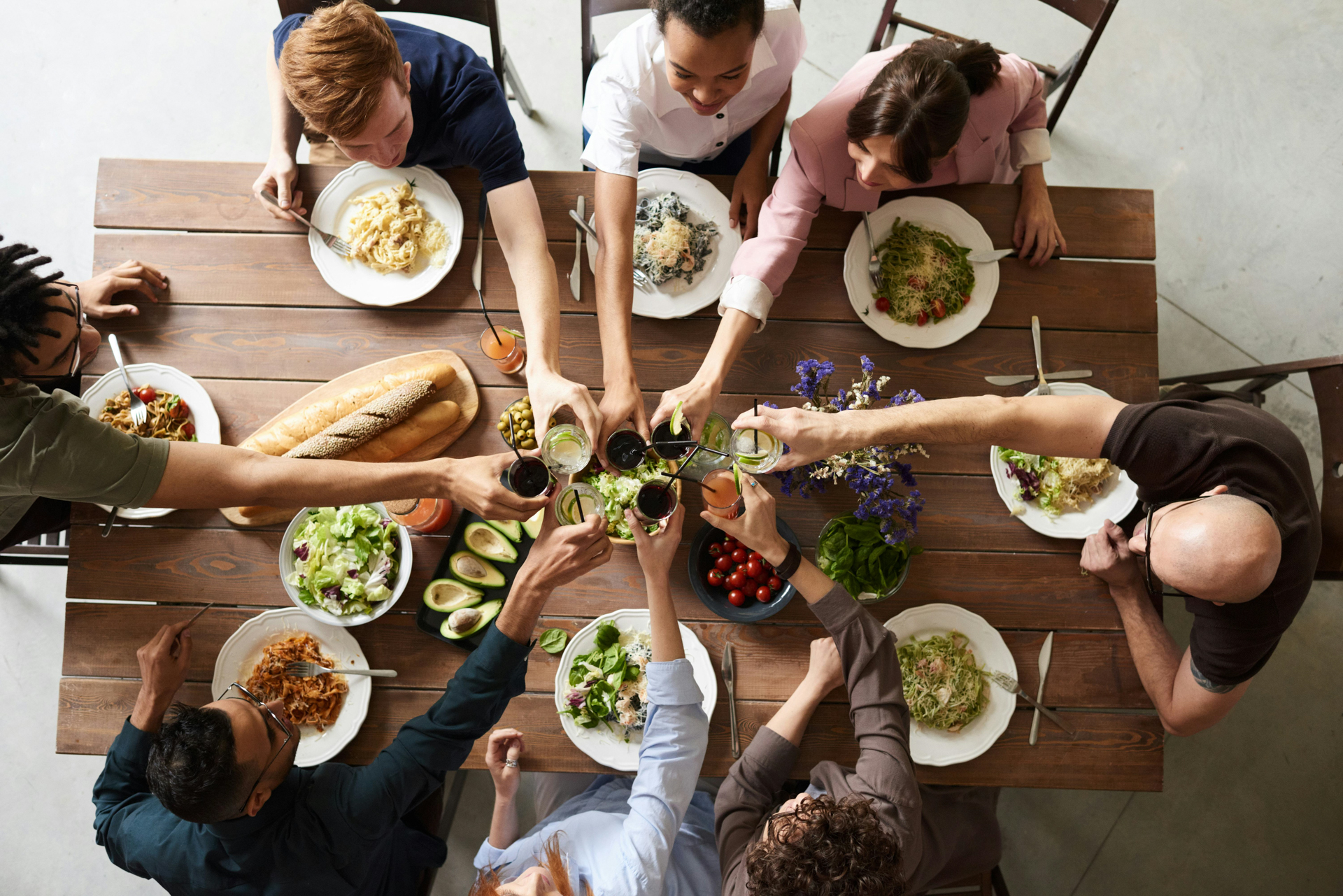 Overhead view of a diverse group sharing healthy salads, bread, and drinks in a communal toast—illustrating What Makes the 90‑Day Intensive Unique in personalized coaching through community, accountability, and holistic wellness