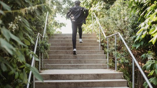 How to break free from limiting patterns: man running up outdoor stairs surrounded by greenery, symbolizing building momentum and overcoming barriers through functional fitness.