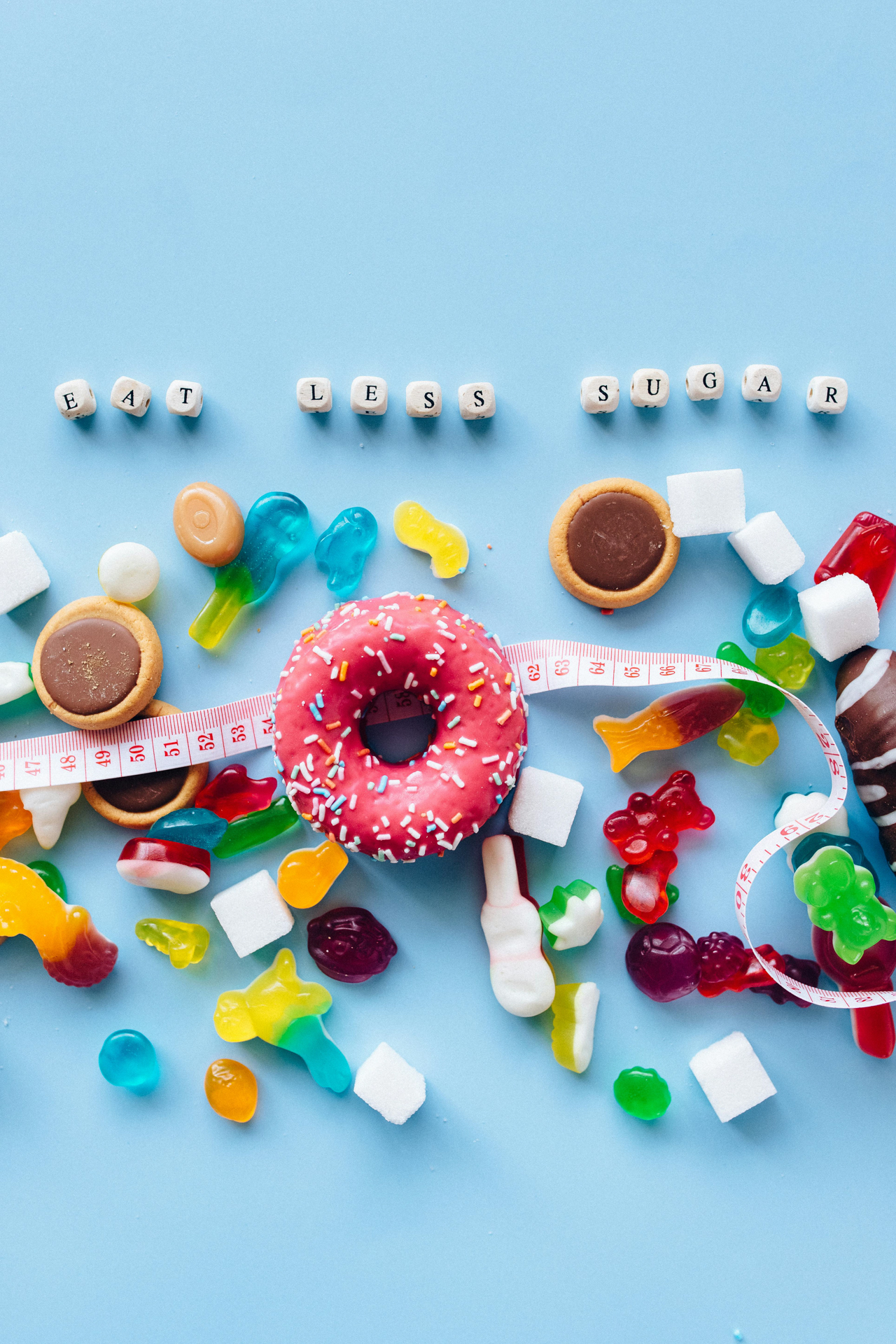 Candy and sweets with a donut and tape measure on a blue background, symbolizing the need to eat less sugar for better blood sugar and insulin resistance.