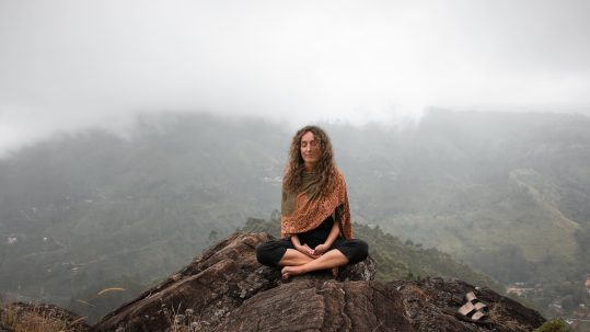 Woman meditating on a mountaintop, symbolizing natural blood pressure management through mindfulness and calm.