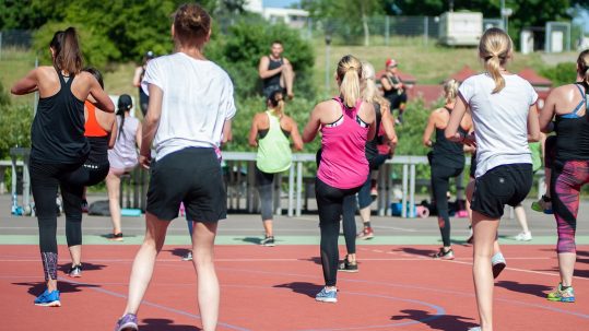 Women exercising outdoors in a group fitness class, performing dynamic movement that balances blood sugar and improves overall metabolic health.
